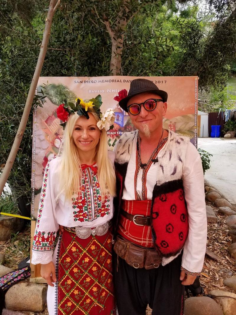 Maria Bobeva and Petro Dushkov in embroidered Bulgarian costumes in front of the Balkan Fest 2017 banner