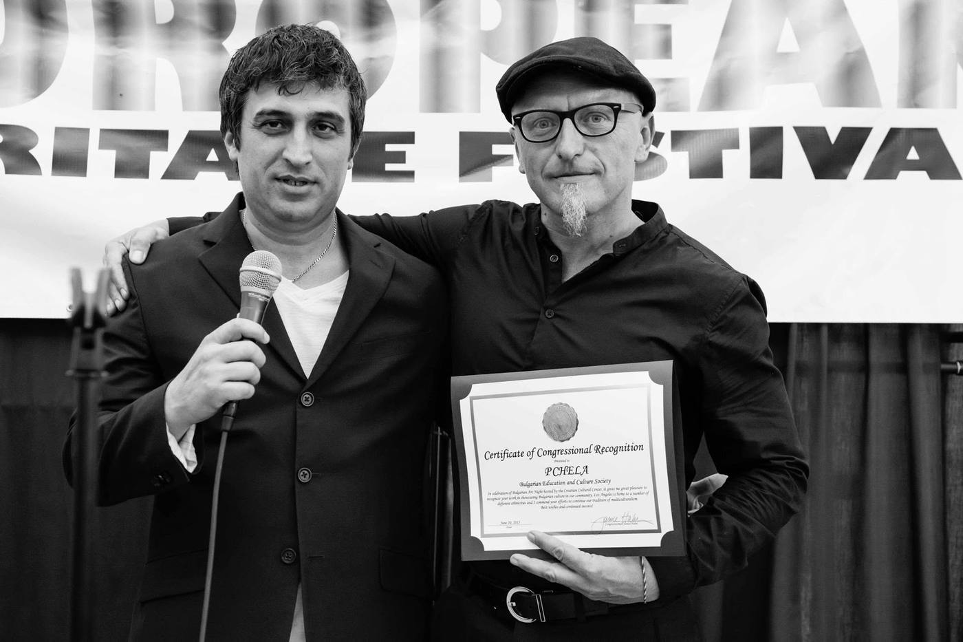 Two PCHELA organizers on stage, one holding a microphone and the other a Certificate of Congressional Recognition